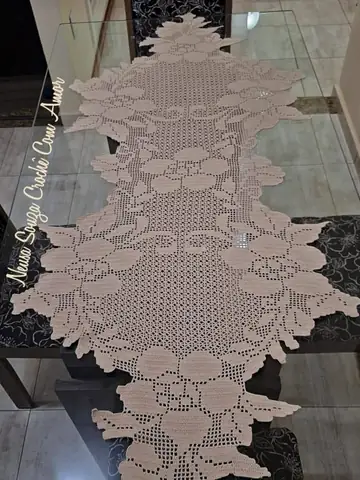 Caminho de mesa rosê de crochê filet com flores, sobre mesa de vidro