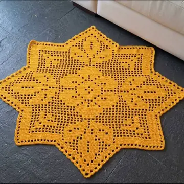 Tapete de crochê filet em forma de estrela, cor mostarda, sobre piso escuro